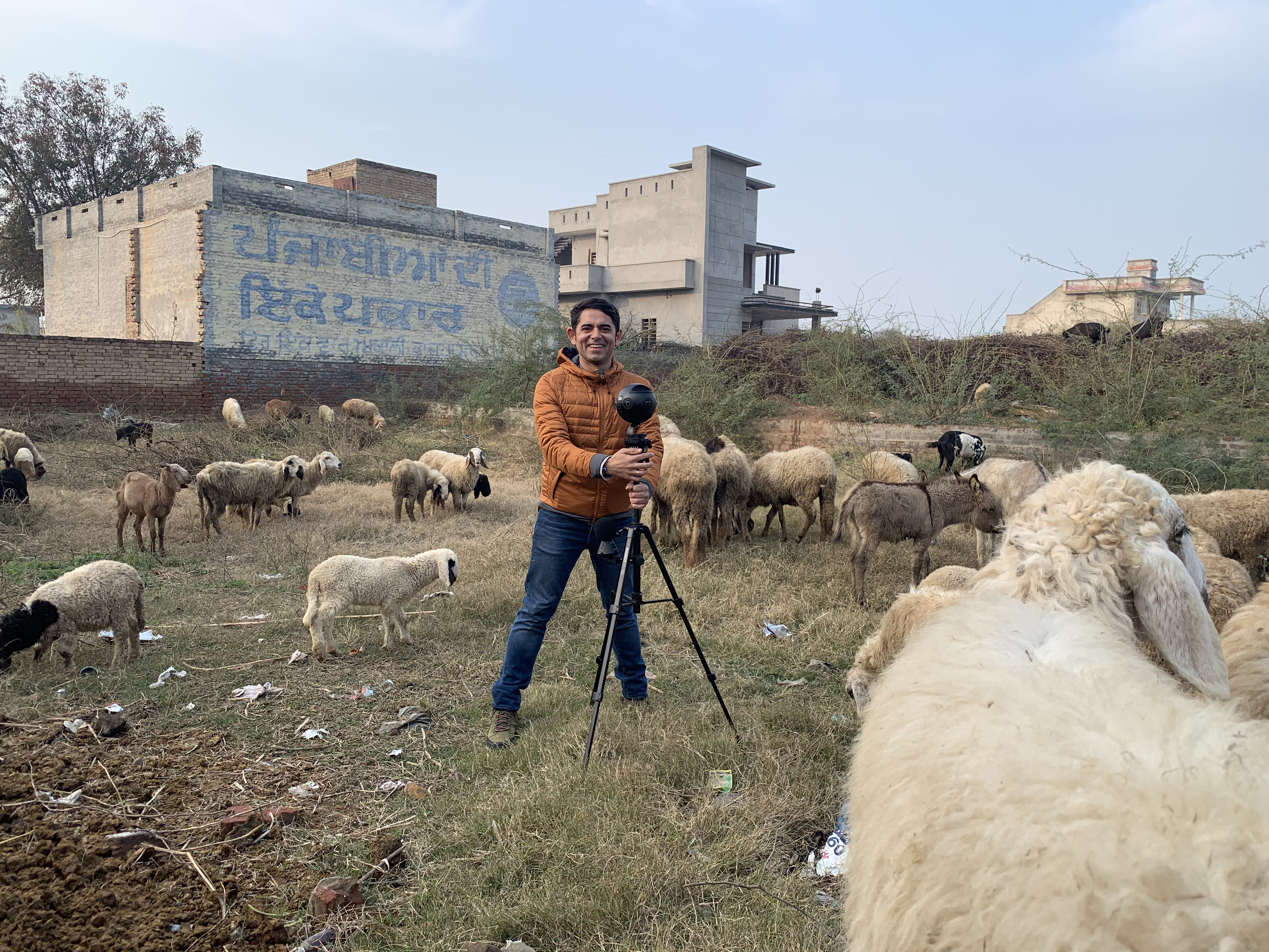 Harjant Gill stands with a tripod in a field with sheep