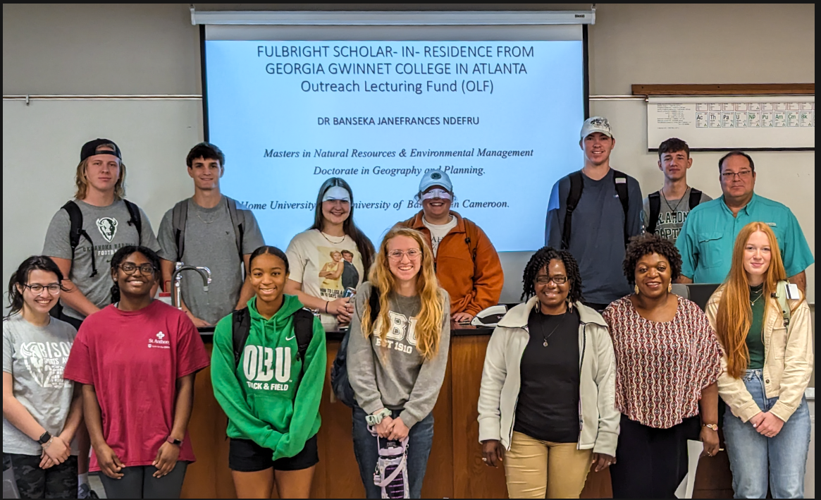 15 people standing in the front of a classroom with a presentation projected on the wall behind them. The Fulbright scholar is in the bottom row, third from left. 