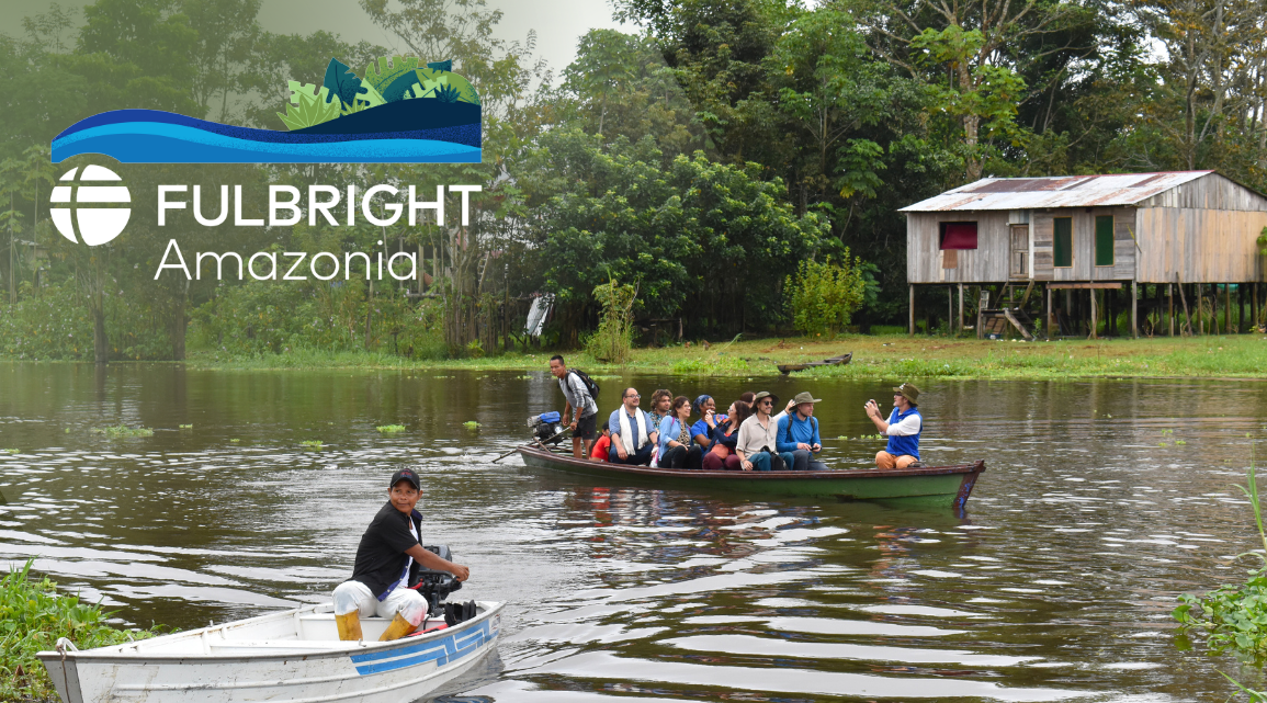 A group of people in a boat on a river in a tropical setting with a wooden house on stilts.