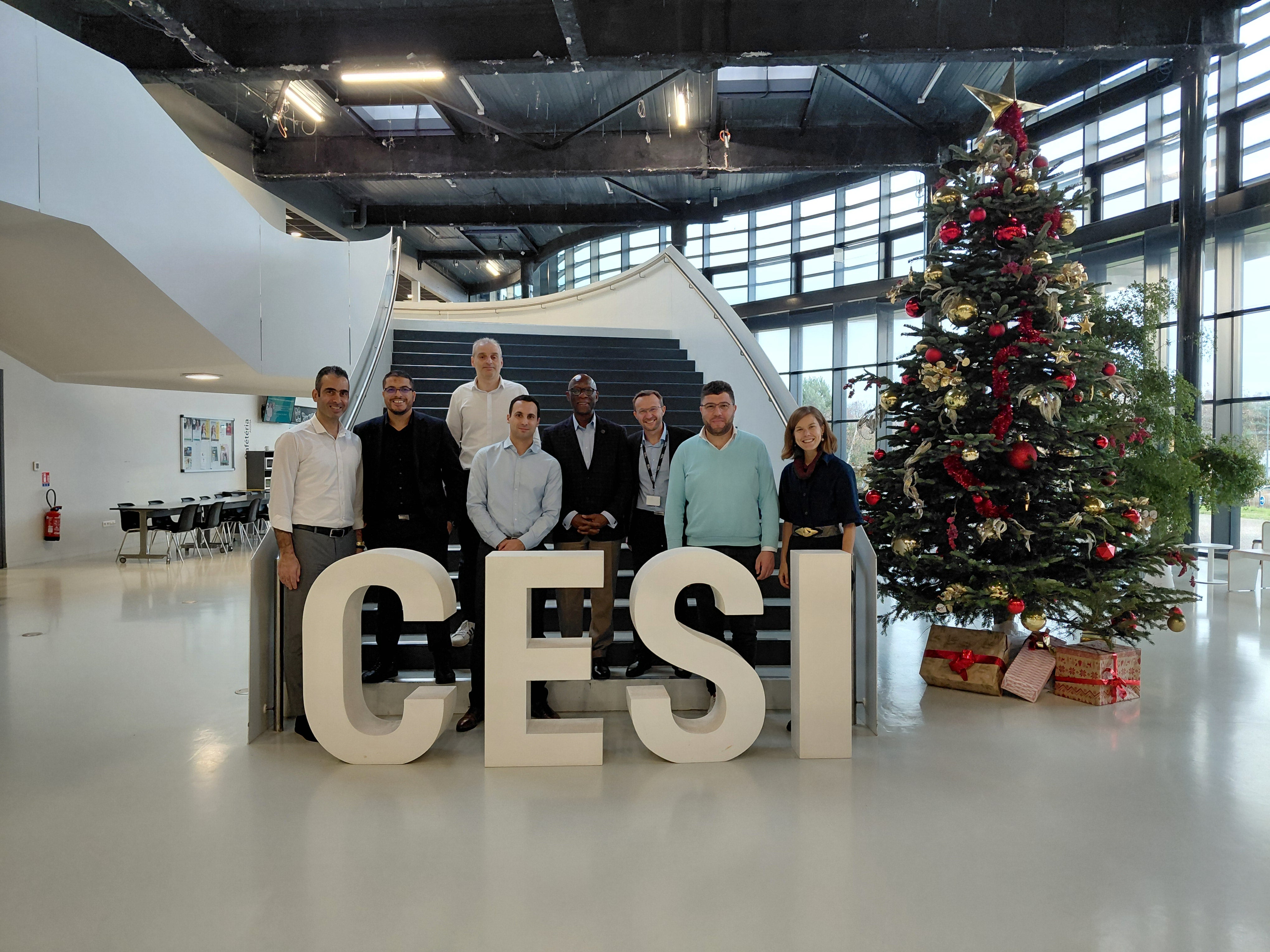 A group of nine people stands behind large letters spelling "CESI" in a modern indoor space with a decorated Christmas tree on the right.