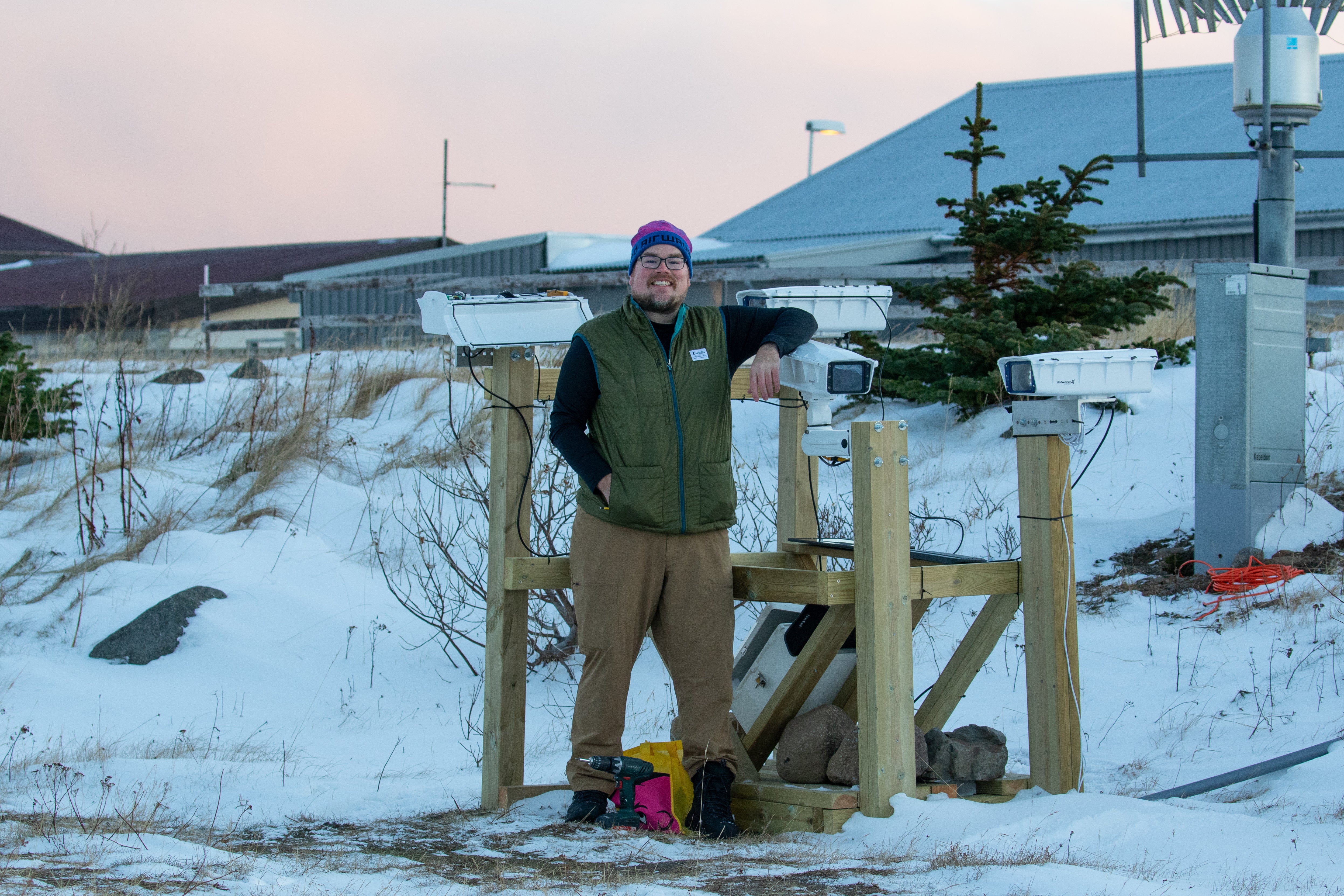 Person standing next to mounted devices in a snowy outdoor setting.