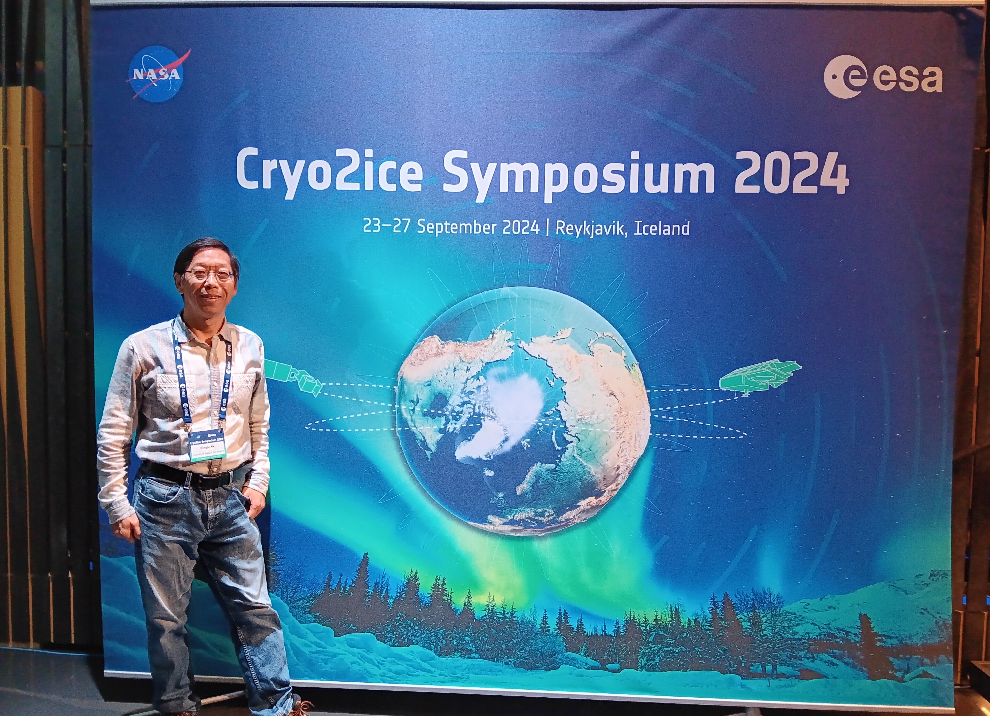 Man standing in front of a Cryo2ice Symposium 2024 backdrop with Earth, aurora, and satellites.