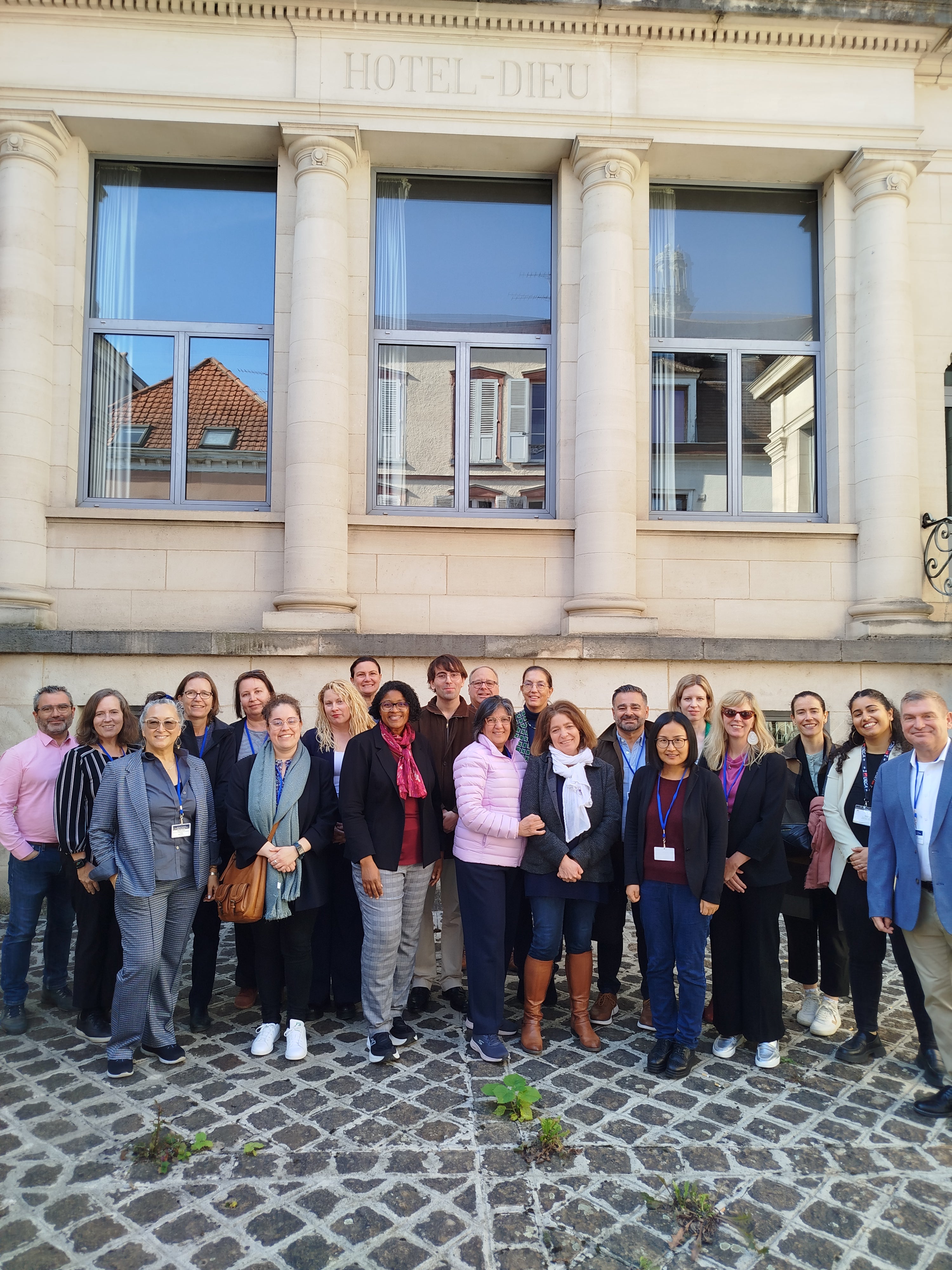 A group of 22 people stands in front of a building labeled "HOTEL-DIEU" with tall columns and large windows.