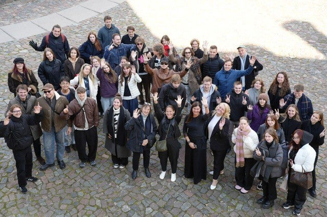 A group of people on a cobblestone surface, waving or raising their hands.