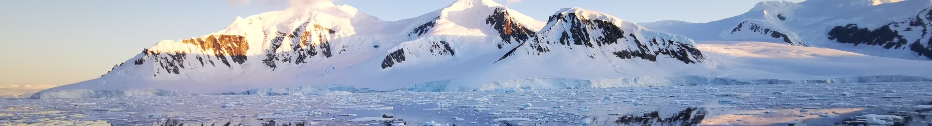 Antarctic mountains with snow and ice reflected on a calm sea.